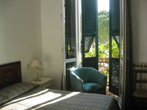 Helles Zimmer im Hotel Beau Rivage in Alassio mit grünen Ladenttüren, die sich zu einem Balkon öffnen und auf üppige Gärten blicken