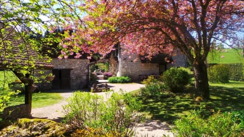 Chaumière en pierre à La Bageatière avec arbres roses en fleur et jardin luxuriant à Lépin-le-Lac