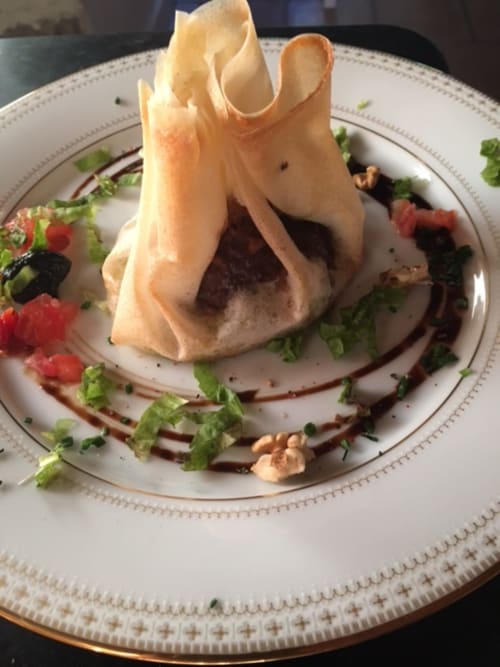 Élégante mise en assiette à La Bageatière : tuile croustillante, mousse sombre, pousses tendres et garniture comestible sur fond blanc