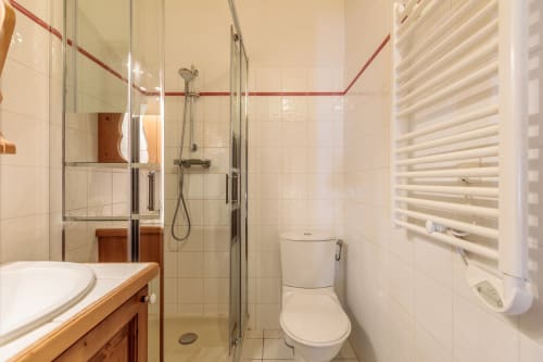 Modern bathroom in Cosyarc apartment with glass shower, wooden vanity, heated towel rack, and white tile finish in