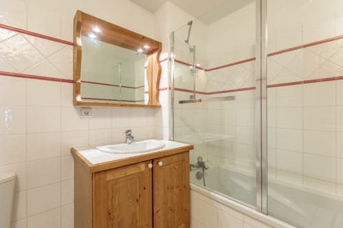 Modern bathroom in the CosyArc apartment in Arc 1800 with bathtub, wooden vanity, white tiles, and lighted mirror