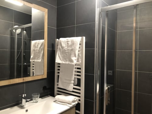 Modern bathroom in Le Champenois apartment at Le château d'Hermonville with black tile walls, wooden mirror frame, and white