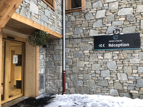 Stone building entrance with 'Réception' sign for Neige & Soleil hotel in Hermonville, snow visible