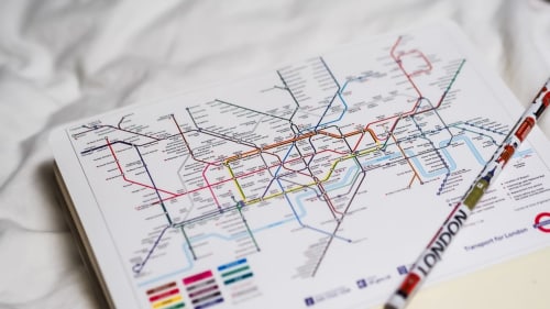 London Underground transit map with colored rail lines and stations on white paper near a pen