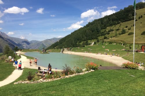 Turquoise alpine lake with sandy beach, mountain valley, and visitors enjoying summer at Hermonville, France