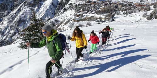 Groupe en raquettes à neige dans les montagnes enneigées près d'Hermonville, France avec un village alpin visible