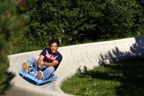 Jeune homme sur luge bleue au château d'Hermonville en Bourgogne, entouré de verdure luxuriante