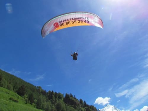 Parapentiste au parachute rouge et jaune survolant une forêt alpine près d'Hermonville, Alpes françaises