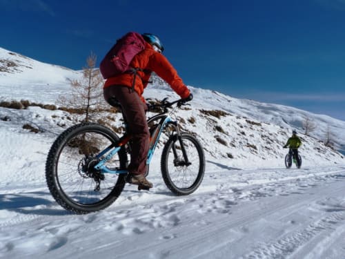 Mountain biker in red jacket riding on snowy trail near Hermonville, France with alpine landscape backdrop
