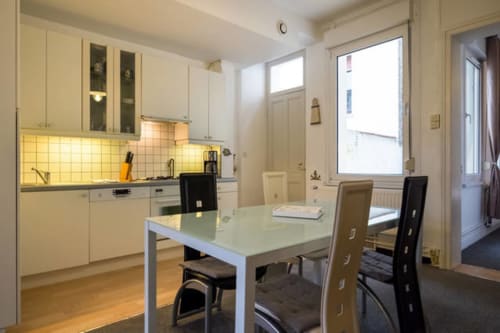Cuisine-salle à manger moderne du gîte Royal Navy à Dunkerque avec placards crème, table et grandes fenêtres