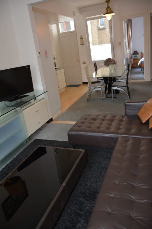 Séjour cottage moderne à Dunkerque avec ottoman en cuir marron, TV écran plat, table à manger et cuisine ouverte