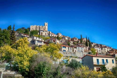 Village médiéval de Banyuls-sur-Mer perché sur une colline avec ses bâtiments en pierre, tour du château, cyprès sous un ciel bleu