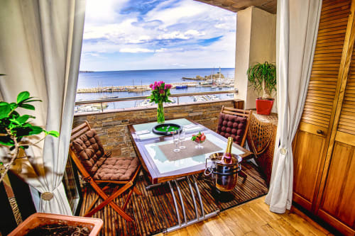 Banyuls-sur-Mer balcony with harbor view, furnished seating, pink flowers, and Mediterranean sea