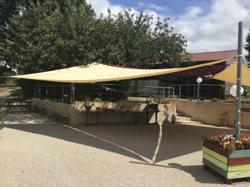 La terrasse extérieure de La Raymondière avec voile d'ombrage jaune, salon de détente et massifs fleuris à Vernoux-en-Gâtine