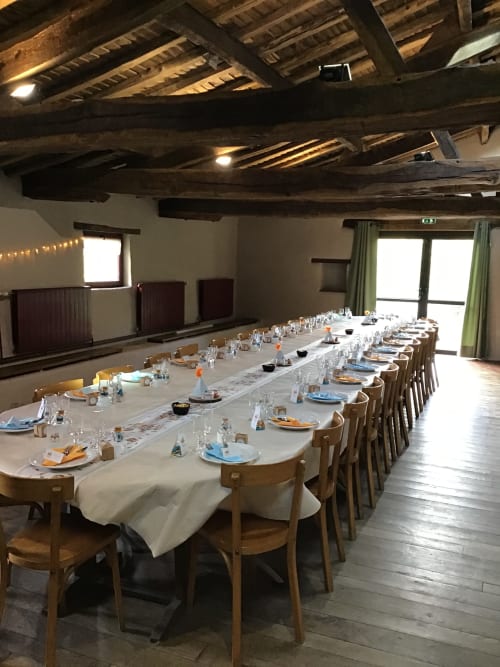 Grande table à manger dressée pour un repas en groupe à La Raymondière, Vernoux-en-Gâtine, avec poutres rustiques et rideaux verts