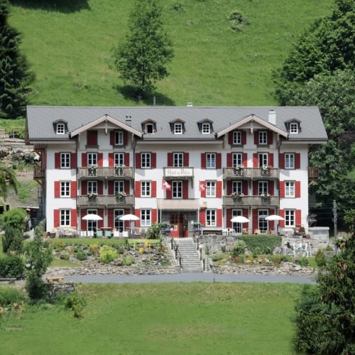 Façade du Historic Hotel du Pillon, grand chalet suisse traditionnel entouré de nature, avec vue dégagée sur les montagnes.