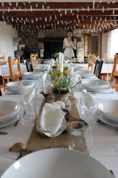 Elegant dining table at Espace Ker Gana with white place settings, succulent centerpiece, and exposed beam ceiling in Plourin