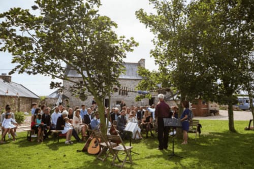 Outdoor gathering at Espace Ker Gana in Plourin with guests seated under trees near stone buildings