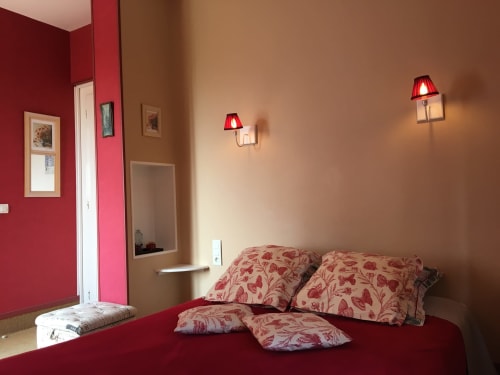 La Chatellenie Standard Room with red bed, floral pillows, and wall-mounted red lamps in Saint Aubin le Cauf