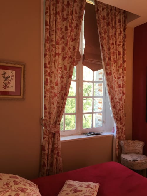 Warm terracotta bedroom with floral curtains, garden view window, and red bedding at La Chatellenie B&B