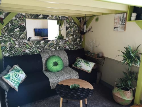 Coin salon confortable chez Orval Et Sens avec papier peint botanique tropical, canapé foncé, accents verts et plantes en pot à Orvault