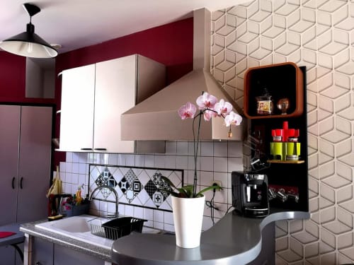 Cuisine moderne de l'hôtel Orval Et Sens avec murs bordeaux, crédence géométrique, orchidées et étagères corail à Orvault