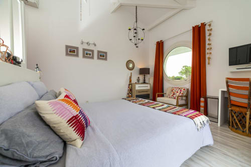 Chambre moderne et lumineuse à l'hôtel Cote Et Dune avec lit double, coussins colorés, baie vitrée ronde avec vue océan et boiseries
