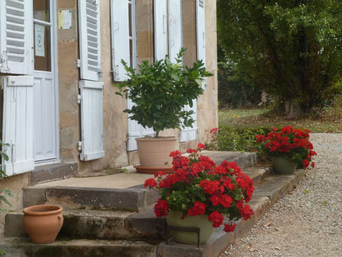 Entrada del Château de Clusors con geranios rojos y contraventanas blancas en Saint-Menoux, Francia