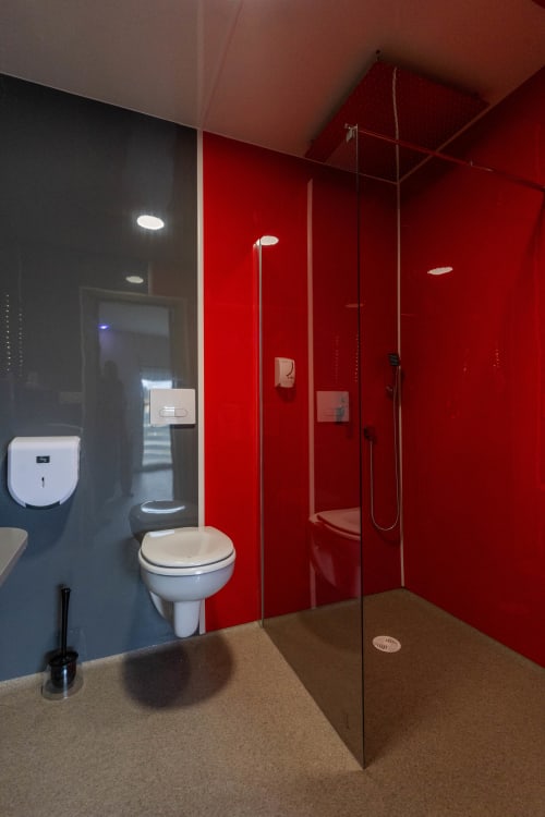 Bany modern de l'Hôtel Rocade a Pamiers amb parets vermelles, mampara de dutxa de vidre, vàter i sòl beix