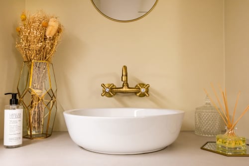 Élégant lavabo de la salle de bains de l'Hôtel Residence Europe & Spa avec vasque blanche, robinetterie en laiton, fleurs séchées et articles de toilette