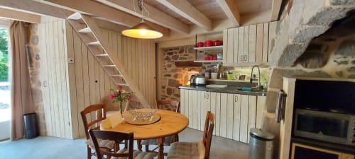 Cuisine rustique et salle à manger avec cheminée en pierre, poutres en bois et table ronde au Mas De Rigoulac