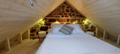 Chambre cosy sous les combles avec murs en pierre, poutres apparentes et éclairage chaleureux au gîte Le Mas De Rigoulac à Argences-en-Aubrac
