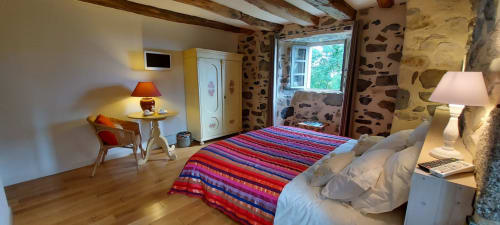 Chambre lumineuse au Mas De Rigoulac avec literie aux rayures colorées, poutres en bois, murs en pierre et vue sur le jardin