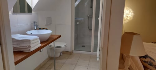 Salle de bain moderne au Mas De Rigoulac avec lavabo rond, douche, toilettes et serviettes blanches sur étagère en bois