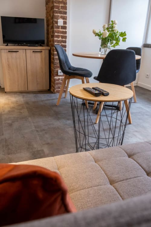 Espace de détente moderne dans la chambre Désiré Dihau au B&B Le Pignié avec table en bois, chaises noires, télévision et colonne en brique