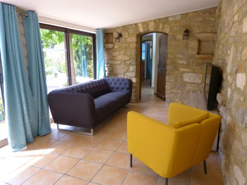 Modern lounge at Villa Thébaïde B&B in Laudun L'Ardoise with yellow chair, dark sofa, stone walls, and garden views