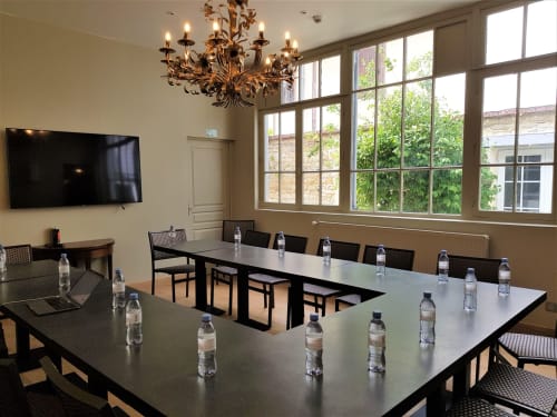Modern meeting room at Les Cabines hotel in Houlgate with large windows overlooking gardens, long black tables, and ornate