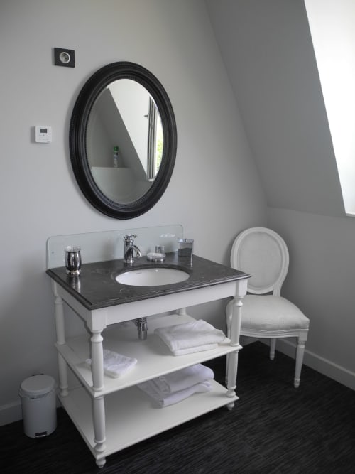 Modern bathroom vanity with black oval mirror and white chair at Le château d'Hermonville B&B in Hermonville, France