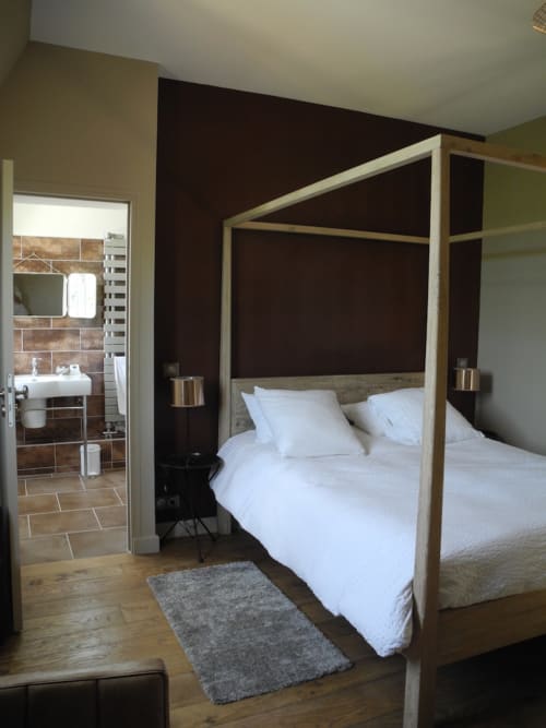Modern bedroom with wooden four-poster bed, white linens, and en-suite bathroom at Le château d'Hermonville, Hermonville.