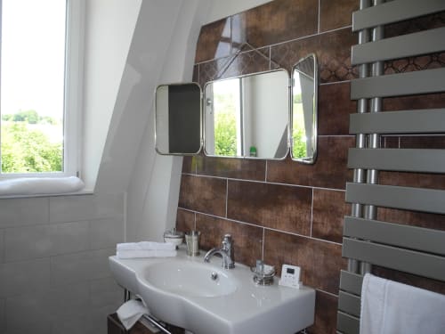 Modern bathroom at Le château d'Hermonville with white sink, brown tile backsplash, and triple mirror cabinet in Hermonville,