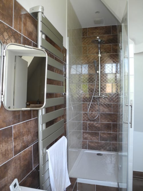 Modern bathroom at Le château d'Hermonville B&B with brown tile shower, rainfall showerhead, and heated towel rack