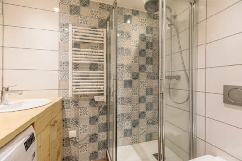 Salle de bains moderne avec carrelage motifs à la douche, meuble vasque en bois et sèche-serviettes électrique dans un appartement de ski résidence Bellecôte-ARC 1800- 