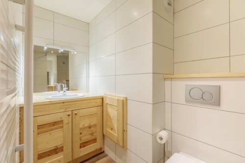 Salle de bain moderne dans un appartement de ski à Bourg-Saint-Maurice avec vanité en bois, grand miroir et carrelage blanc
