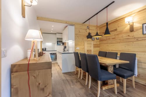 Cuisine et salle à manger d'appartement de ski moderne aux murs en bois, cuisine équipée, table à manger avec chaises noires et suspension