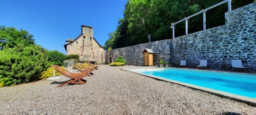 L'espace piscine du Mas De Rigoulac avec bâtisse en pierre, chaises longues et vue sur la campagne de l'Aubrac
