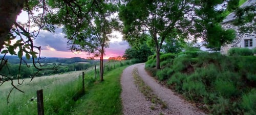 Vue au coucher de soleil d'une allée de gravier bordée d'arbres menant au Mas De Rigoulac à Argences-en-Aubrac