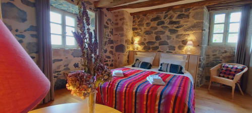 Chambre douillette au Mas De Rigoulac avec murs en pierre, literie rayée colorée et vue sur le jardin à Argences-en-Aubrac