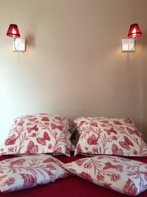 Elegant bedroom at La Chatellenie with red botanical bedding, decorative wall lamps, and garden view in Saint Aubin le Cauf