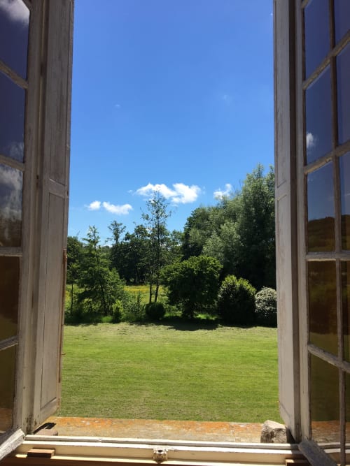 Open doors framing lush garden view at La Chatellenie Grace Apartment in Saint Aubin le Cauf