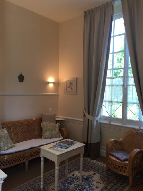 Grace Apartment sitting area at La Chatellenie B&B with garden view through tall windows, wicker furniture and elegant décor